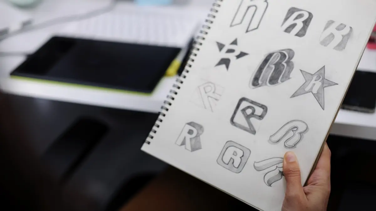 Szkice logo z literą R w szkicowniku obok tabletu graficznego